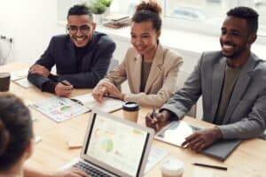 three coworkers sit at a table and actively listen to a fourth coworker.