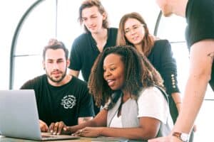 woman explaining concept at desk with team crowded around her