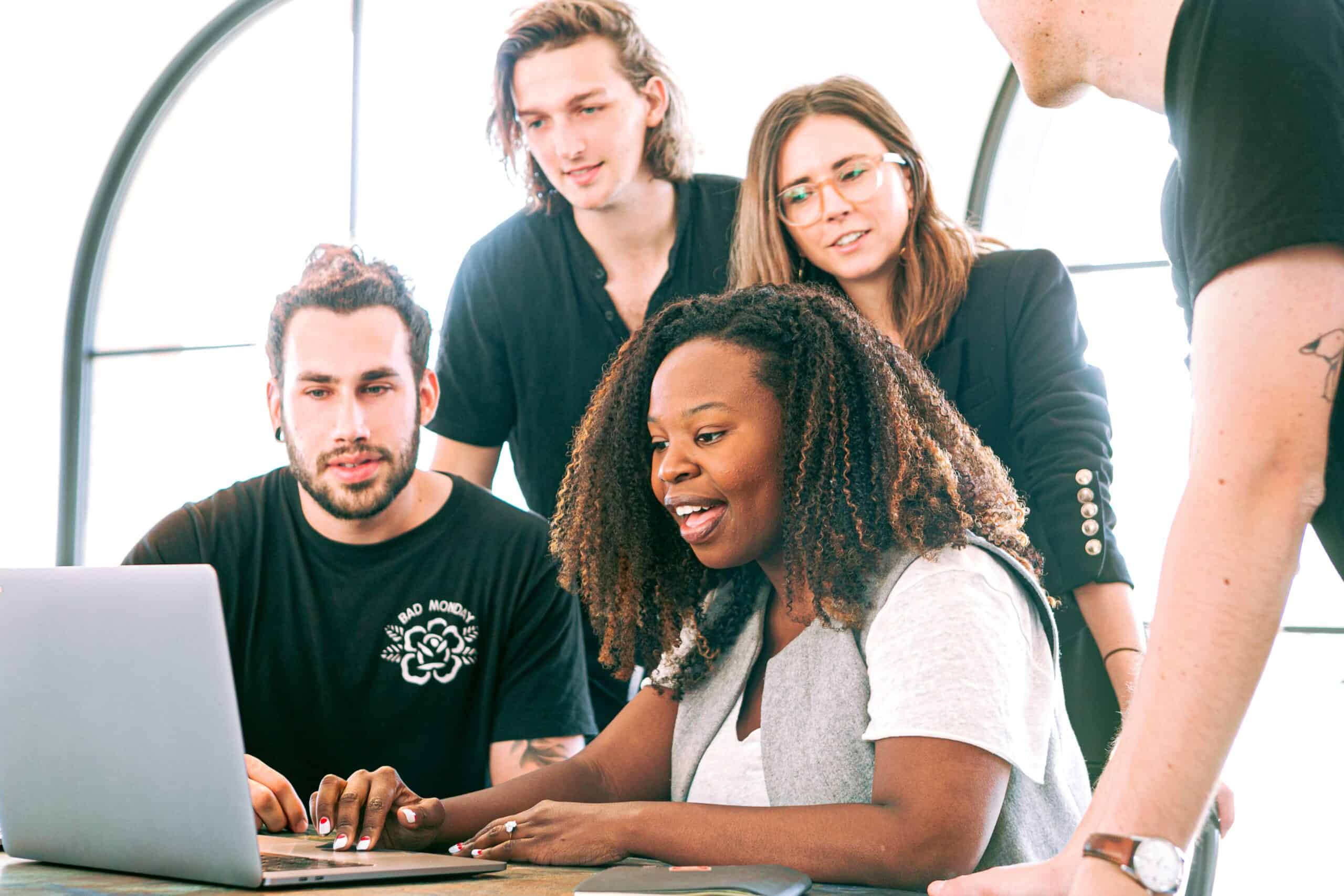 woman explaining concept at desk with team crowded around her