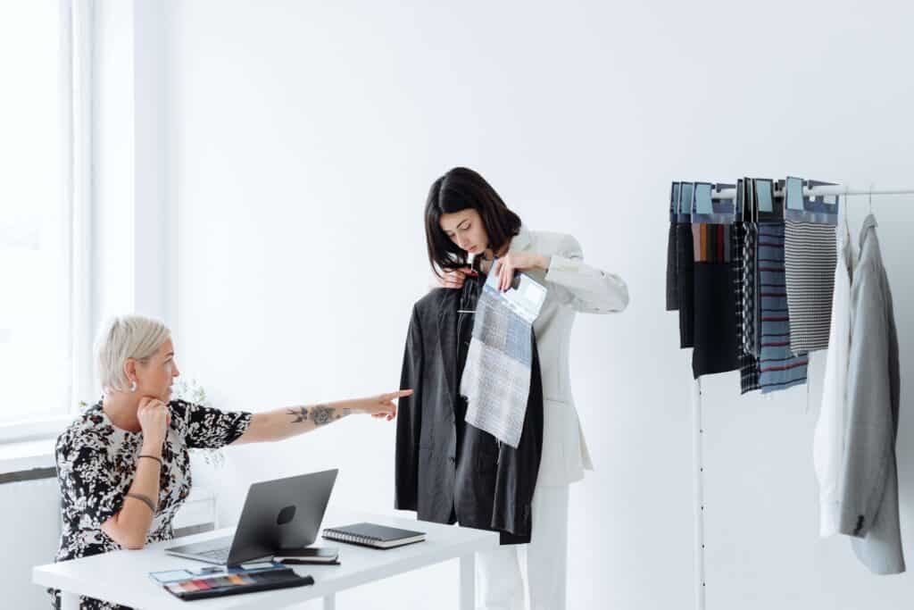 woman holding up business casual clothes while other woman points at clothing item