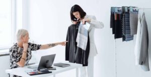 woman holding up business casual clothes while other woman points at clothing item