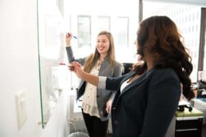two women in front of a dry erase board