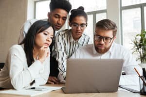 A group of young professionals collaborate at a computer in an office