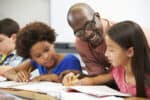 Teacher Helping Pupils Studying At Desks In Classroom